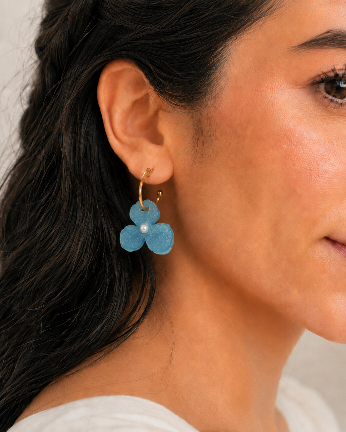 Detalle del arete Aura Celeste puesto, flor azul brillante con perla y aro dorado