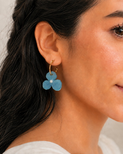 Detalle del arete Aura Celeste puesto, flor azul brillante con perla y aro dorado
