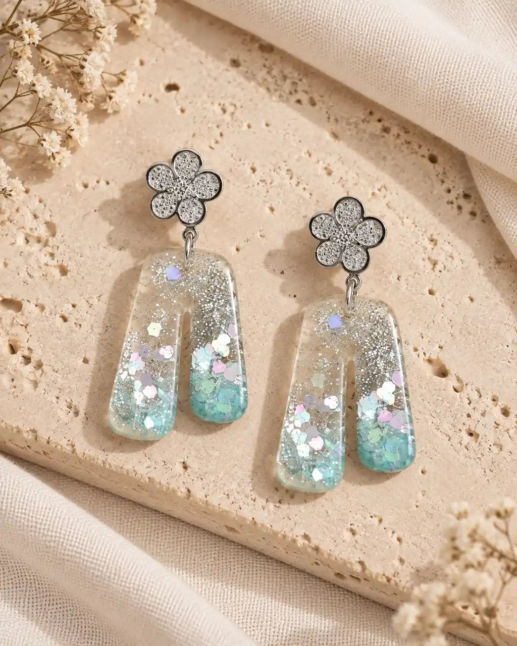 Aurora Clara, par de aretes de flor plateada y arco translúcido sobre travertino