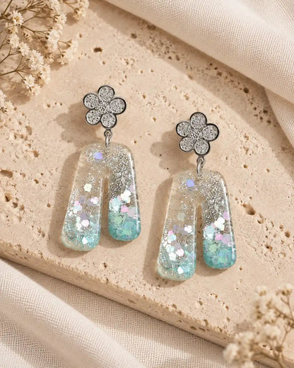 Aurora Clara, par de aretes de flor plateada y arco translúcido sobre travertino