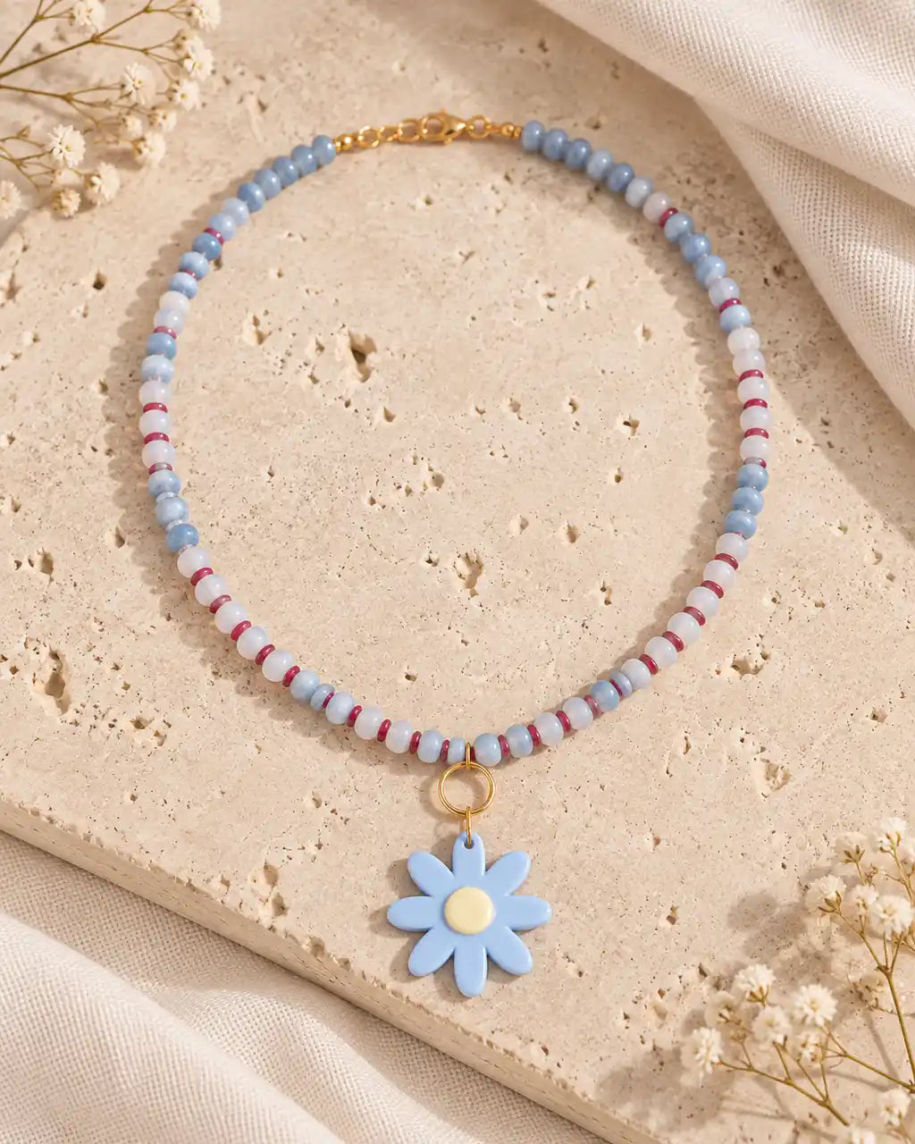 Margarita Celeste, collar corto de cuentas azules y flor azul sobre travertino