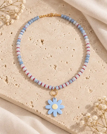 Margarita Celeste, collar corto de cuentas azules y flor azul sobre travertino