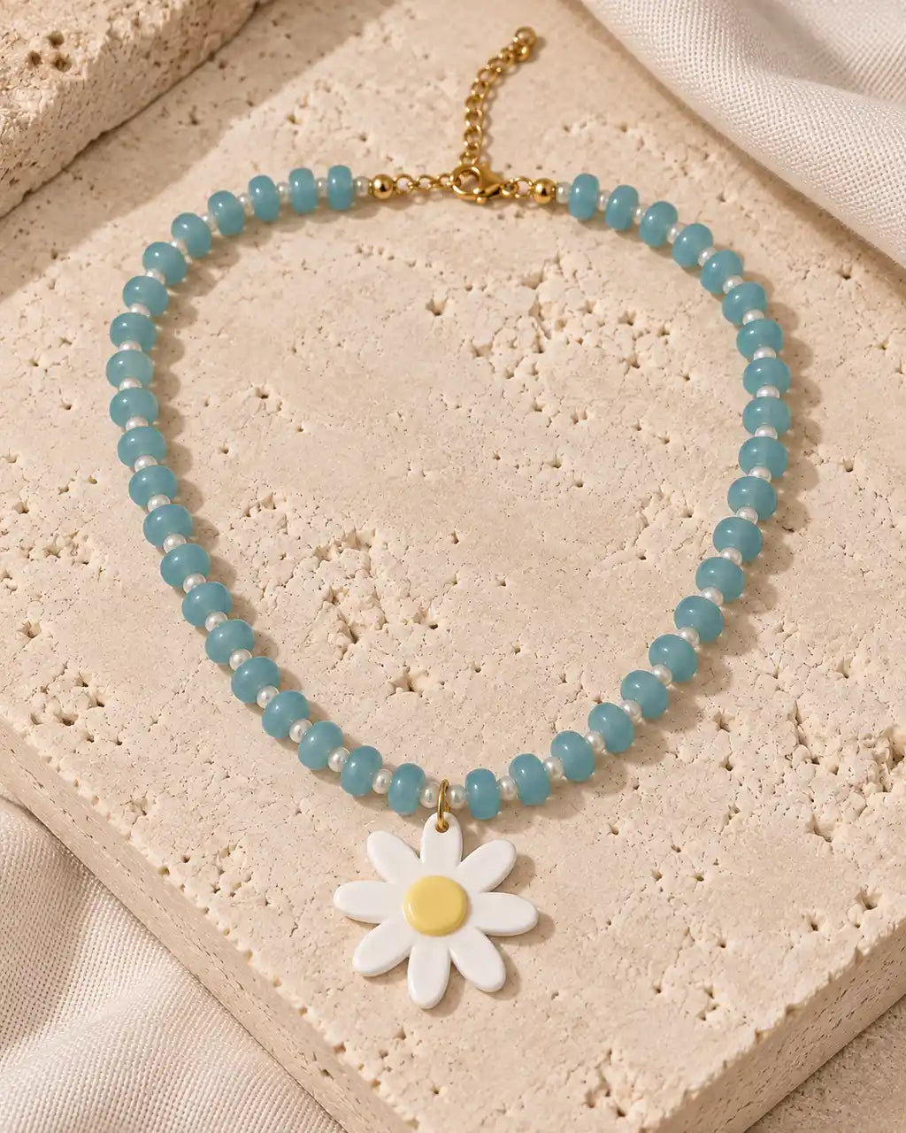 Brisa Margarita, collar aqua con flor blanca y centro amarillo sobre travertino