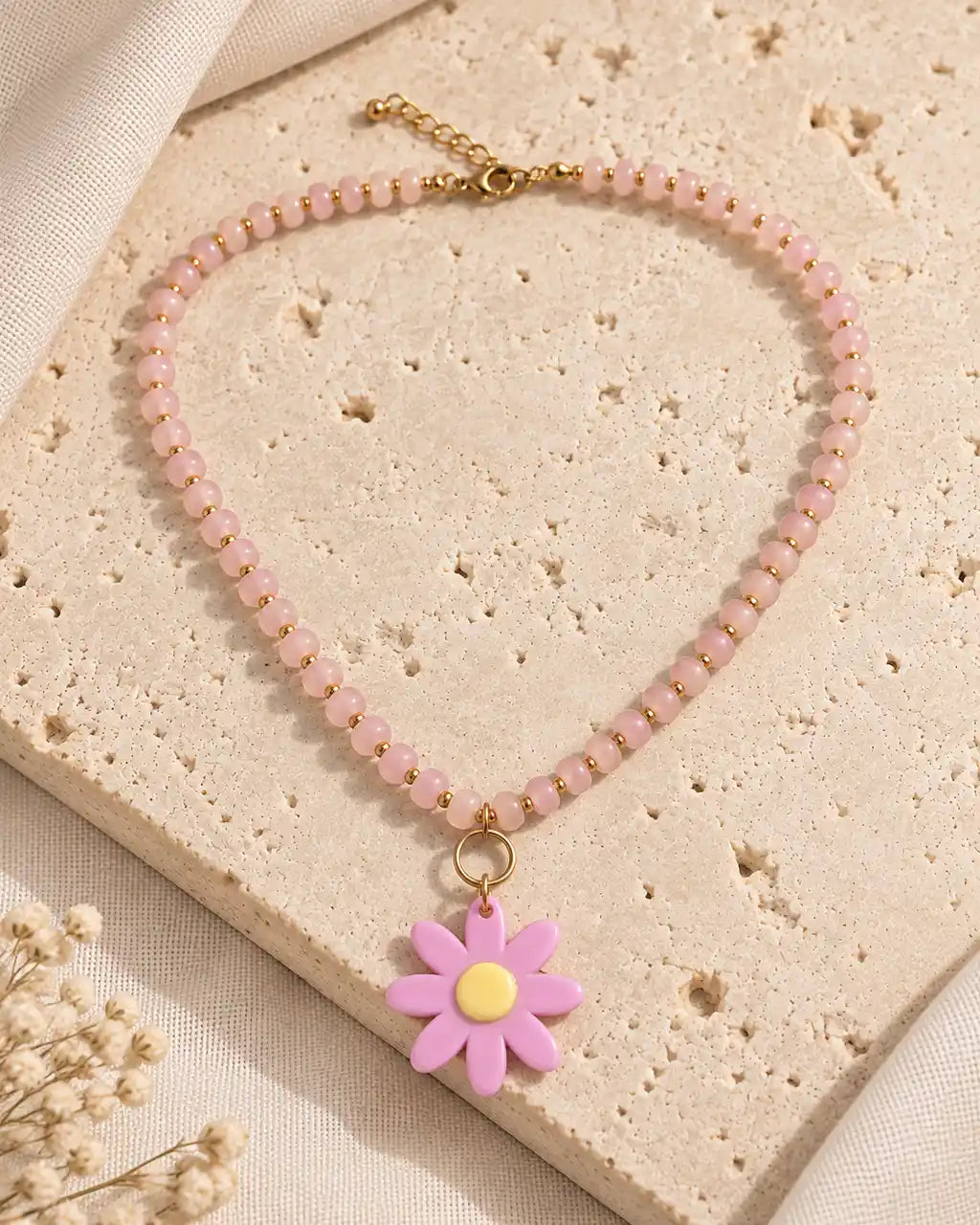 Rosa Silvestre, collar rosado con margarita de centro amarillo sobre travertino